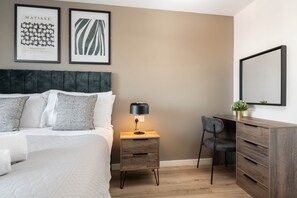 A bedroom with a bed, bedside table, lamp, chair, dresser, and two framed artworks on the wall. - Richmond Row 2 Bed Apartment (203) | Secure Parking & EV (Liverpool)