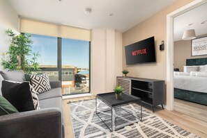 A modern living room with a sofa, a coffee table, a TV mounted on the wall, and a large window offering a view of the outside. - Richmond Row 2 Bed Apartment (203) | Secure Parking & EV (Liverpool)