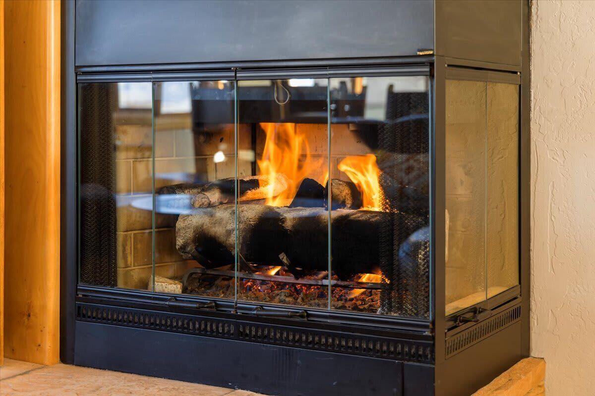 A fireplace with a glass front, visible fire, and a stone base.
