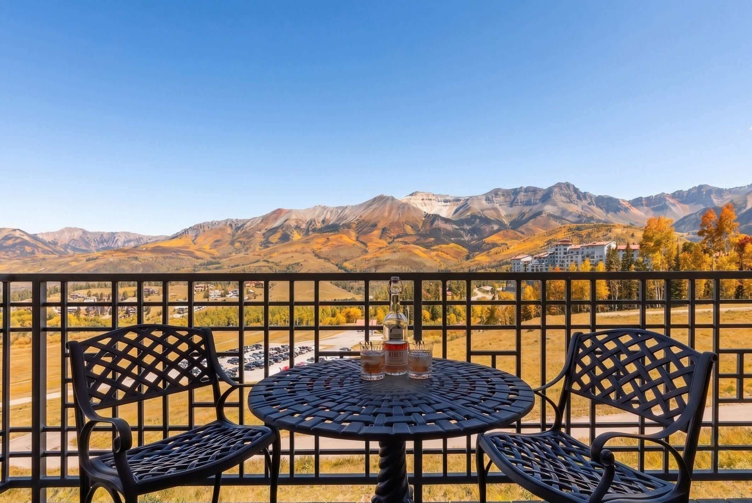 A balcony with a table and chairs, overlooking a mountainous landscape.