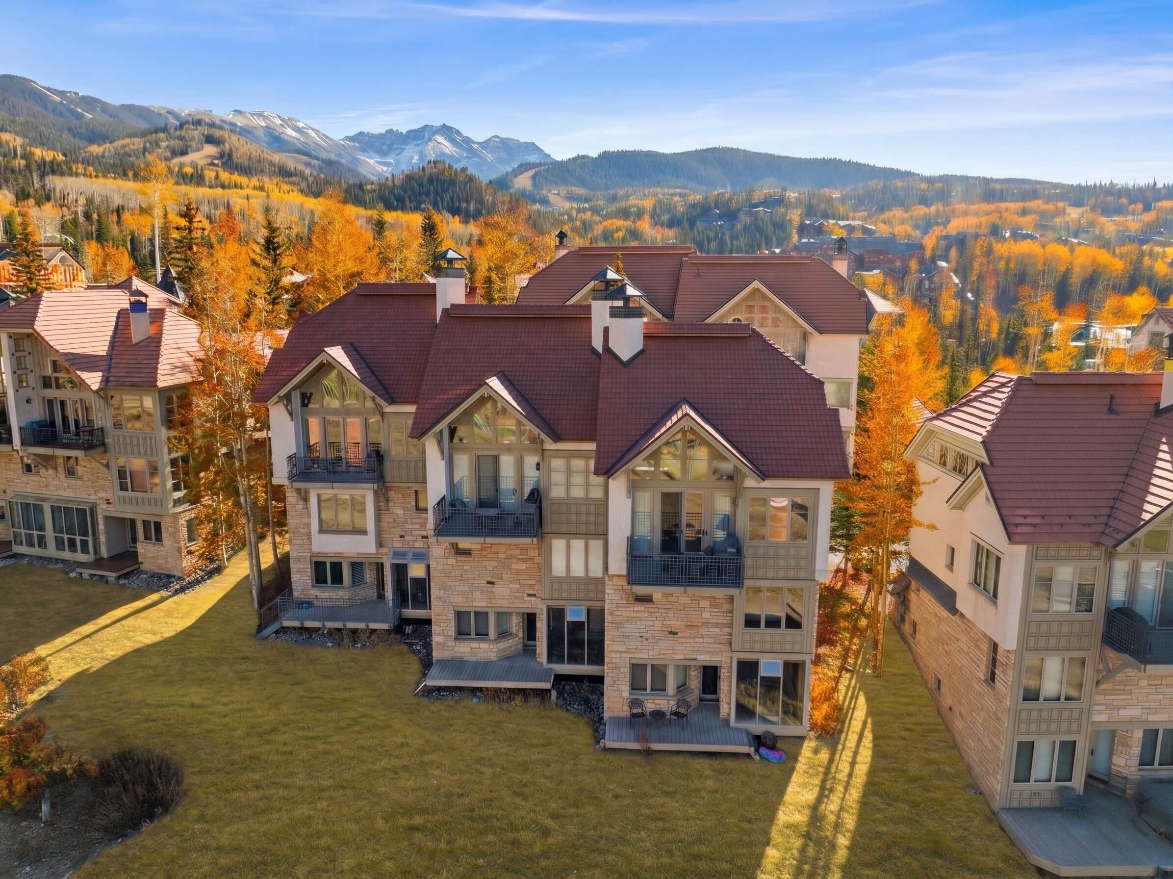A multi-story residential building with a stone facade, multiple balconies, and a view of a mountainous landscape.