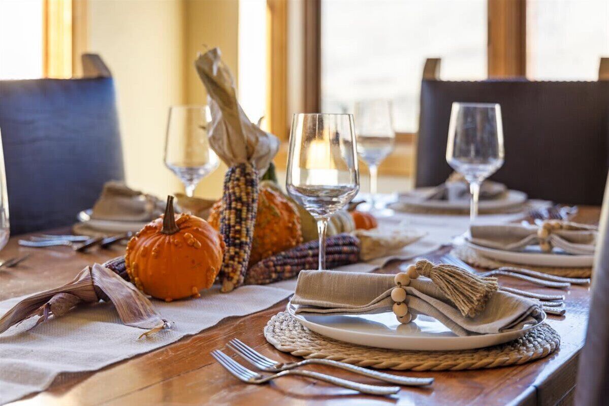 A dining table set with plates, glasses, and a centerpiece of pumpkins and corn.