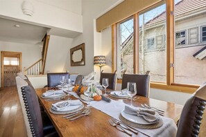 Ein Essbereich mit einem Holztisch, gedeckt für sechs Personen, Stühlen, einer Lampe und Blick auf ein Gebäude.