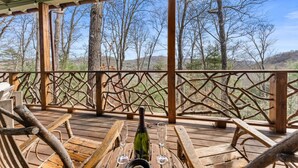 Eine Holzterrasse mit rustikaler Geländer, eine Champagnerflasche und zwei Gläser auf einem Holztisch.
