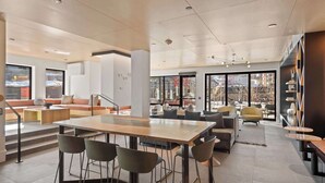 Un interior espacioso y moderno con zona de comedor central, asientos cómodos y grandes ventanales que ofrecen vistas al exterior.