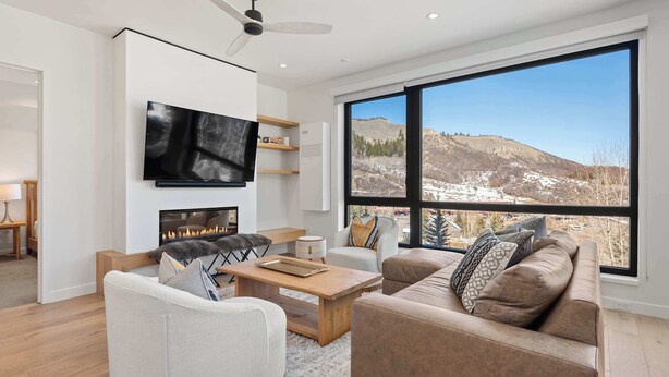Una sala de estar moderna con chimenea, asientos cómodos, un televisor grande y vistas a un paisaje montañoso.