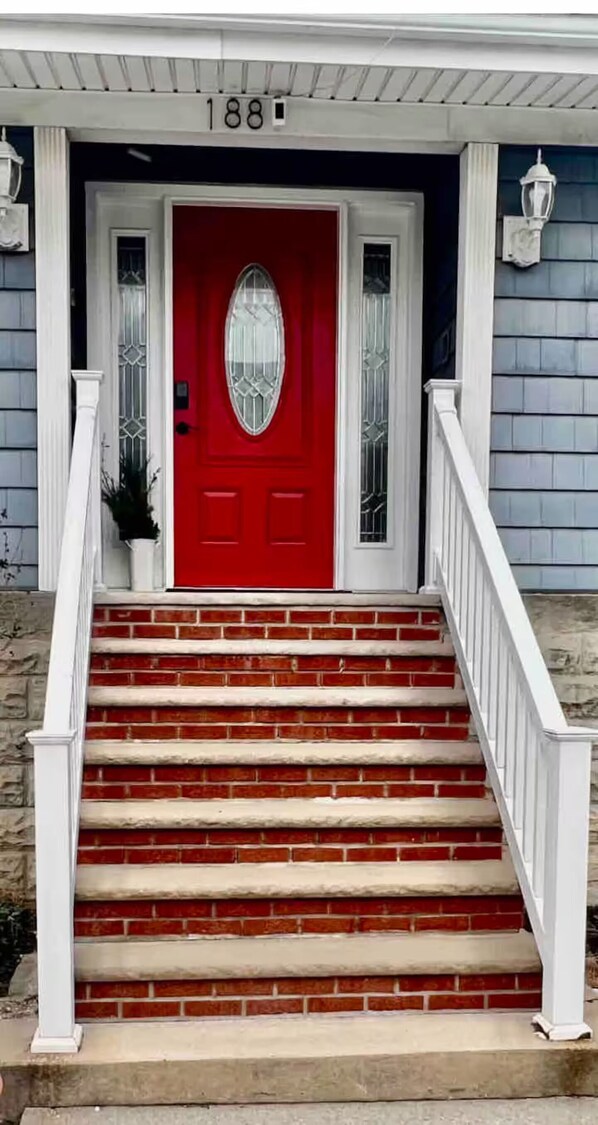 A red door with a white porch and a brick staircase leading up to it.