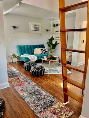 A modern living room with a teal sofa, black and white patterned cushions, a glass coffee table, and a colorful rug.
