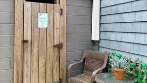 A wooden door with a sign, a wicker chair, and a potted plant in a courtyard. - Private Charming 2 bedroom steps from the beach
Entire rental unit in Queens, NY (Rockaway Beach)