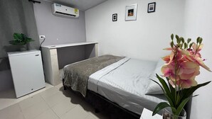 A compact hotel room with a bed, a desk, a small refrigerator, and an air conditioner. - CASAMARTINA (Cartagena)