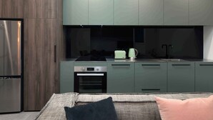Une cuisine moderne avec des meubles de couleur sombre, un four encastré et un réfrigérateur en acier inoxydable.