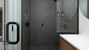 Une salle de bain moderne avec une douche à l’italienne en verre, un lavabo blanc et un miroir.