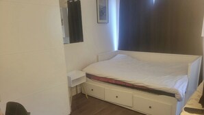 Une chambre avec un lit simple, une table de chevet, une chaise et une armoire.