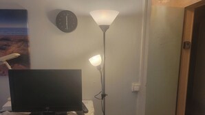 Une pièce avec une télévision posée sur une table, un lampadaire et une horloge au mur.