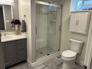 A modern bathroom with a glass shower enclosure, a white toilet, and a grey vanity with drawers. - Cozy & Modern 3-Bed Getaway Near Lake Erie (Bay Village)