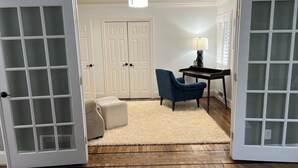 Ein Zimmer mit Holzboden, einem blauen Sessel, einem kleinen Tisch mit Lampe und einer weißen Tür mit Glasfeldern.