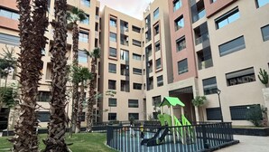 Ein moderner Apartmentkomplex mit mehreren Hochhäusern, einem Spielplatz und Palmen.