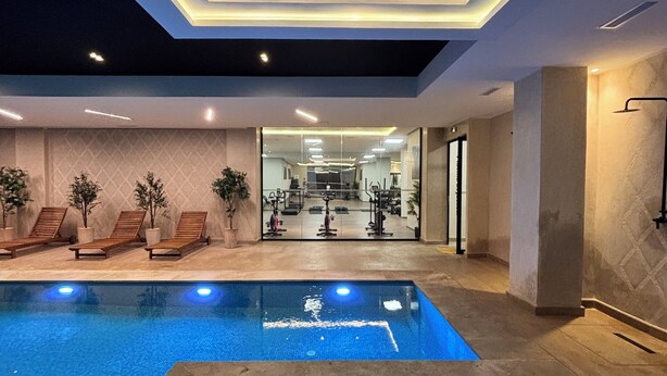 Ein moderner Innenpool mit Whirlpool, Liegestühlen und Blick auf einen Fitnessbereich.