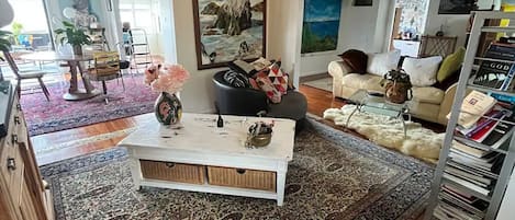 A spacious living room with a large patterned rug, a white coffee table, and a painting of a seascape.