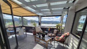 Un espace extérieur abrité, doté d’une structure en verre, d’un plancher en bois et offrant une vue sur le paysage.
