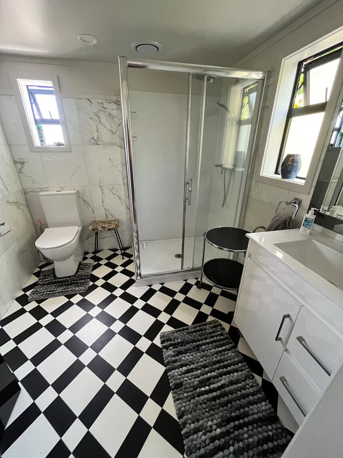 A bathroom with a black and white checkered floor, a glass shower enclosure, a toilet, a sink, and a vanity with drawers.