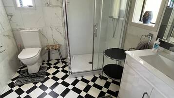 A bathroom with a black and white checkered floor, a glass shower enclosure, a toilet, a sink, and a vanity with drawers.