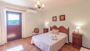 A bedroom with a bed, two bedside tables, a chair, a window with curtains, and a chandelier. - El Acebuche Mijas by Ruralidays (Málaga)