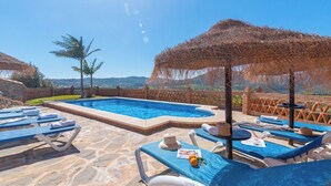 A pool area with lounge chairs and umbrellas, a stone floor, and a view of the landscape. - El Acebuche Mijas by Ruralidays (Málaga)