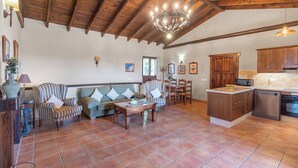 A spacious living room with a sofa, armchairs, and a dining table. A kitchen with wooden cabinets and modern appliances is visible. - El Acebuche Mijas by Ruralidays (Málaga)