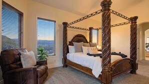 Una cama con dosel de madera y cabecera, un sillón de cuero marrón con un cojín, y un ventanal con persianas.