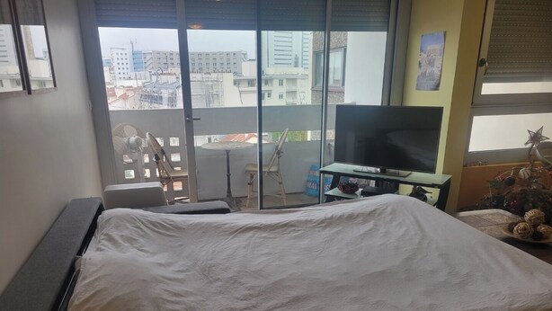 Een hotelkamer met een bed, een televisie, een klein tafeltje en een balkon met uitzicht op de stad.