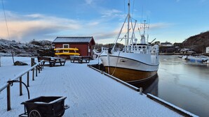 A boat docked at a pier with a snow-covered ground, a small wooden building, and a clear sky. - Stunning apartment in Finnås with house sea view (Finnås)
