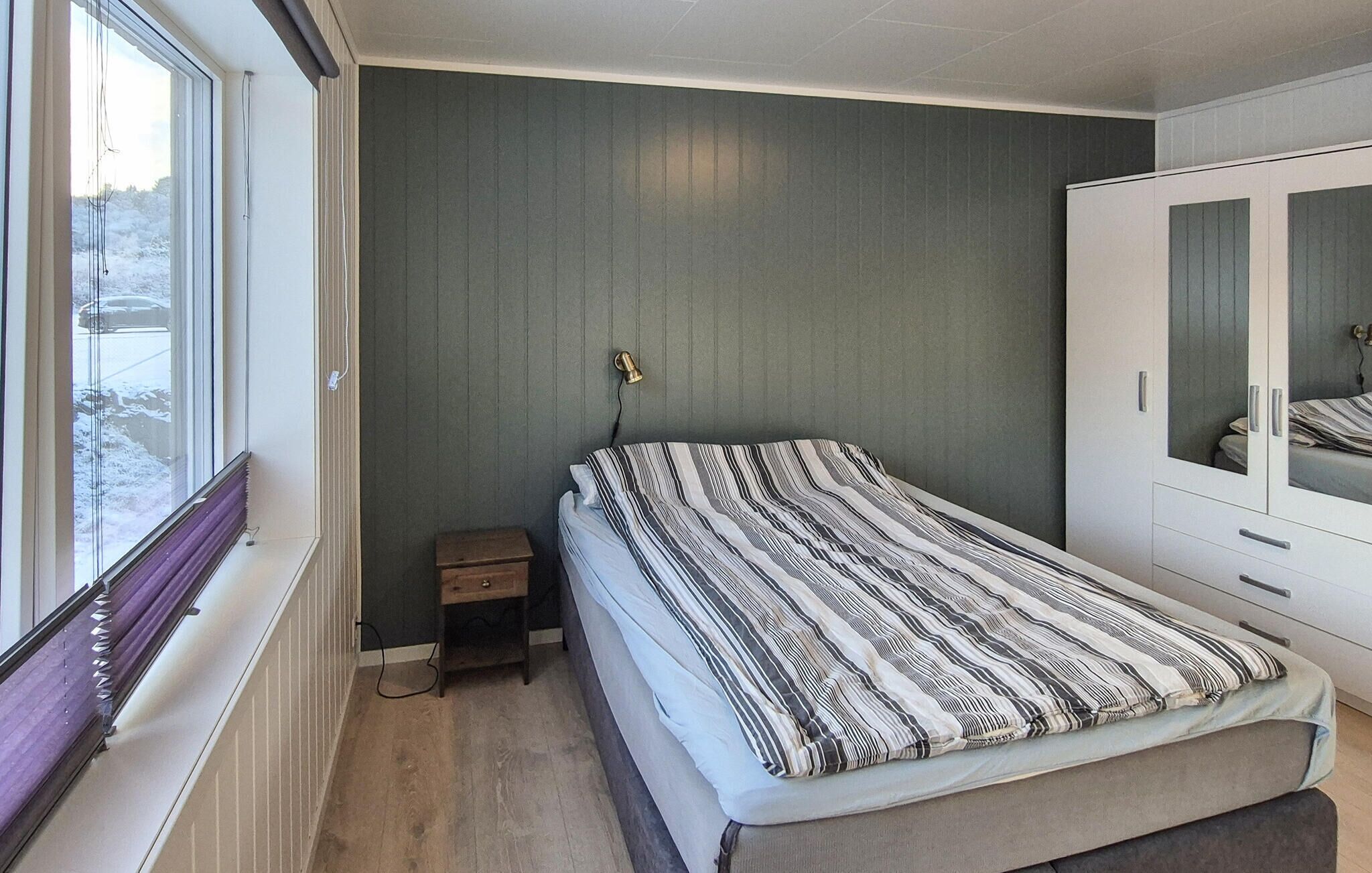 A bedroom with a bed, a small bedside table, a wardrobe, and a window with a view of a snowy landscape.