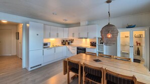 A modern kitchen with white cabinets, a wooden dining table, and a hanging light fixture. - Stunning apartment in Finnås with house sea view (Finn ås)