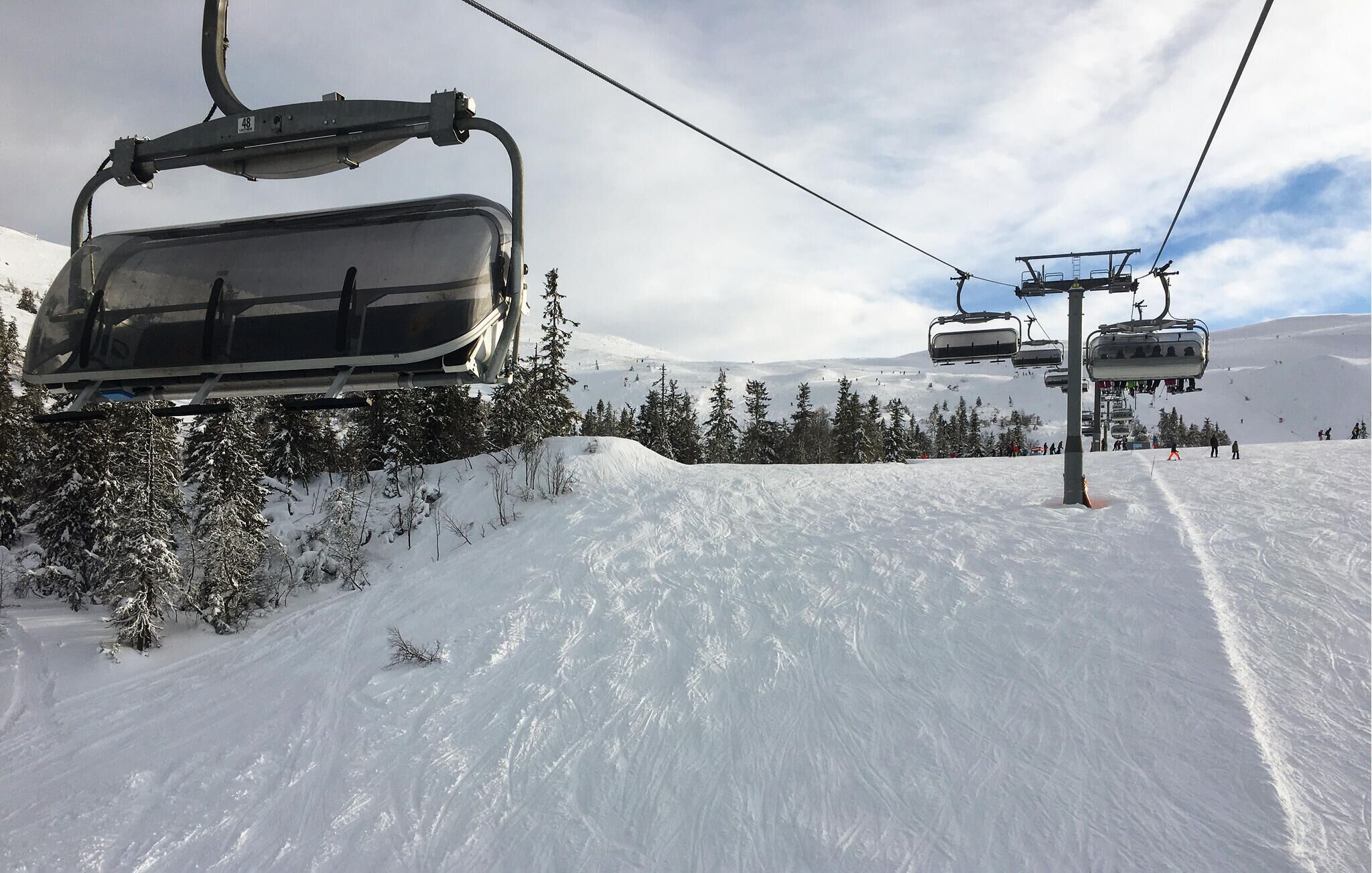 A ski lift with chairs moving along a snowy slope, surrounded by snow-covered trees.