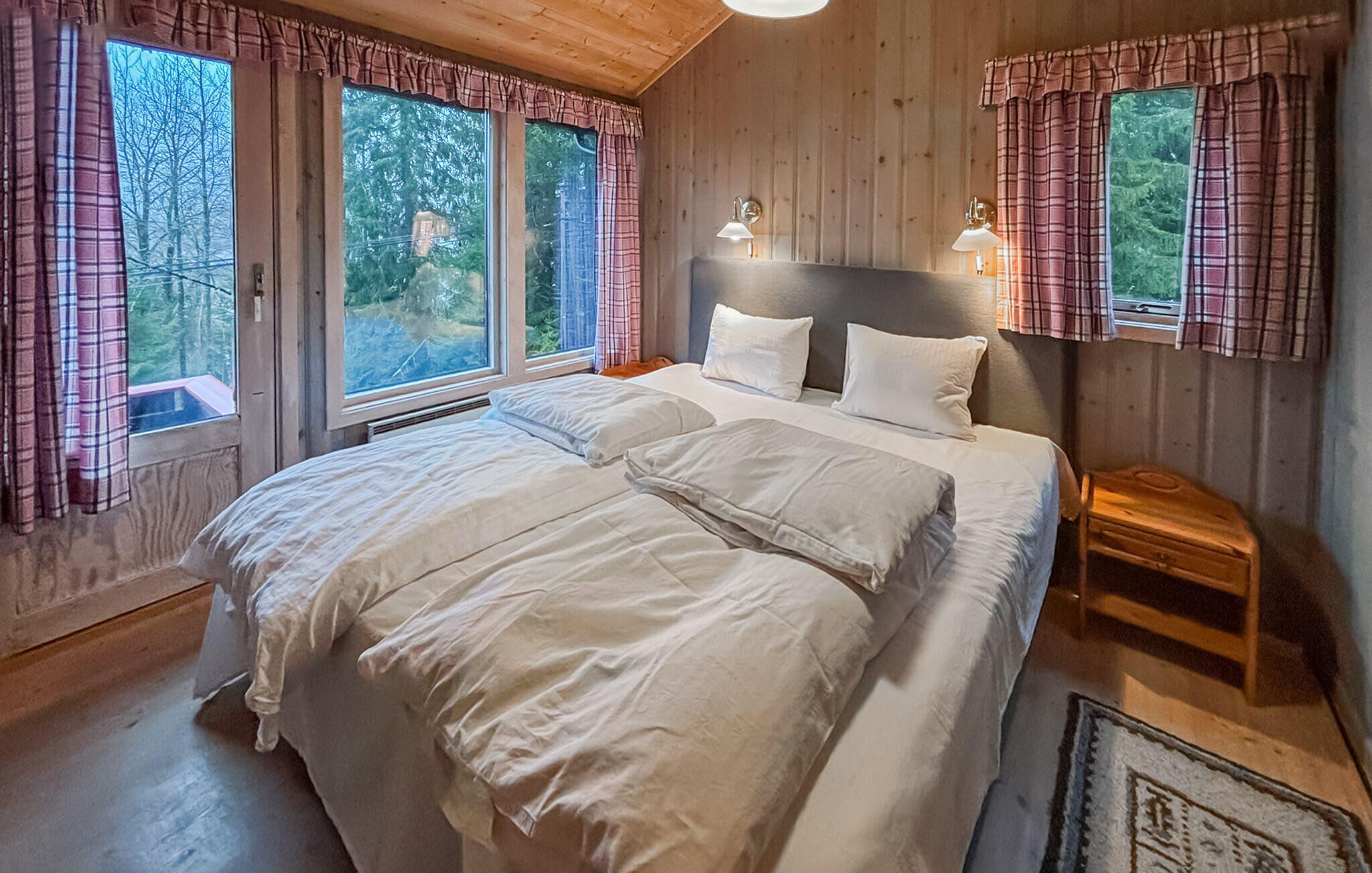 Une chambre à coucher avec un grand lit, deux tables de chevet, une tête de lit et trois fenêtres avec des rideaux.