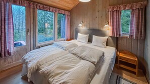 Ett sovrum med en stor säng, två sängbord, en sänggavel och tre fönster med gardiner.