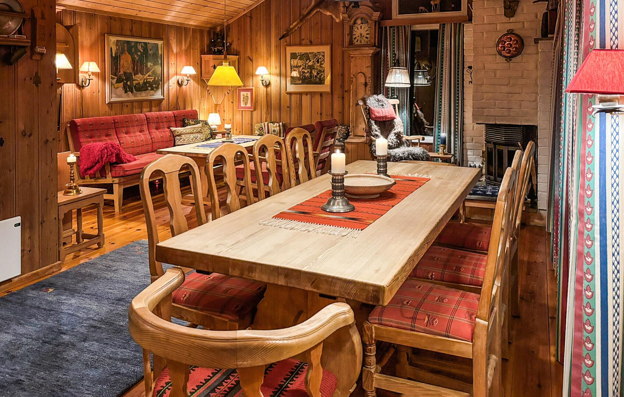 Ett mysigt matrum med träpanel, ett långt bord, rött klädda stolar och en öppen spis.