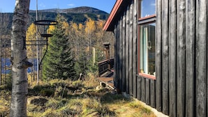 En stuga byggd av trä med utsikt över en skog och berg i bakgrunden.