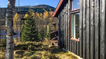 En stuga byggd av trä med utsikt över en skog och berg i bakgrunden.