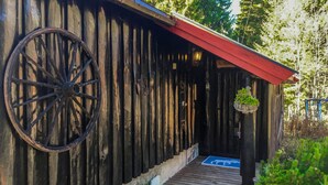 En rustik träbyggnad med ett stort hjul fäst på väggen, ett rött tak och en träveranda som leder till ingången.