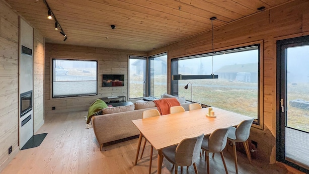 Ein modernes Interieur mit Holzboden, großen Fenstern, einer Couch, einem Esstisch und Stühlen.