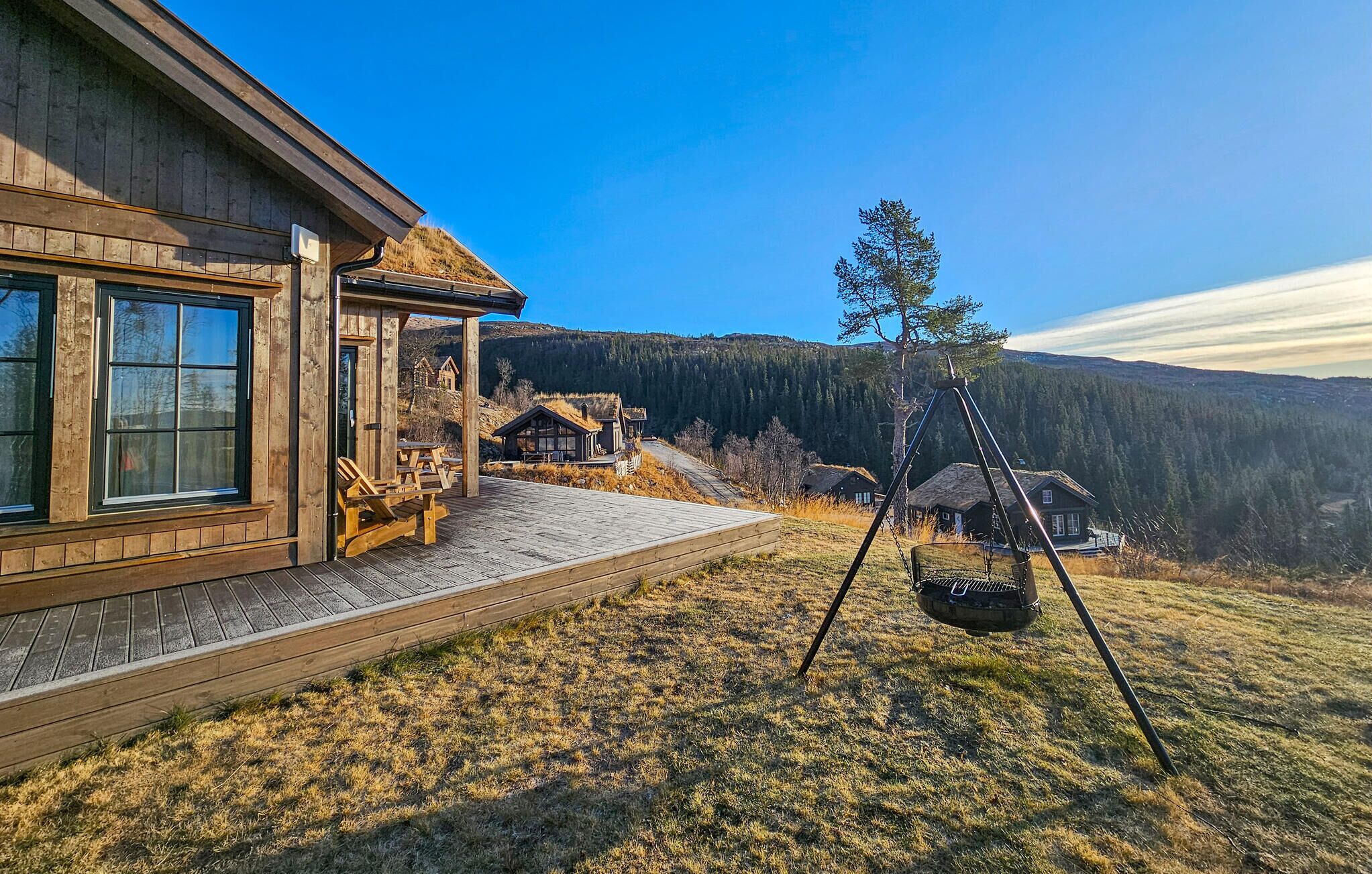 Uma cabana de madeira com varanda, balanço e vista para uma cadeia montanhosa arborizada.