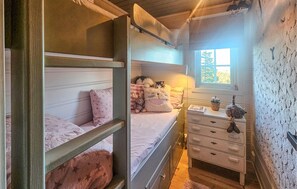 Ein Schlafzimmer mit Etagenbetten, einem Schminktisch und einem Fenster mit Blick auf Bäume.