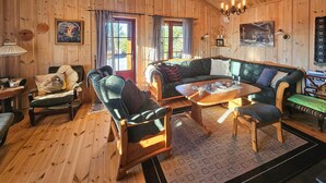 A cozy cabin-style room with wooden walls and floors, featuring a green patterned sofa, a wooden coffee table, and a chair with a cushion. - Stunning home in Austbygda with WiFi (Austbygda)