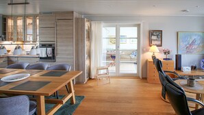 Ett modernt vardagsrum med ett matbord i trä, en soffa och en köksdel med en inbyggd ugn och skåp.