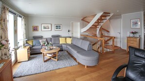Ett vardagsrum med en grå hörnsoffa, en trätrappa och ett trägolv.