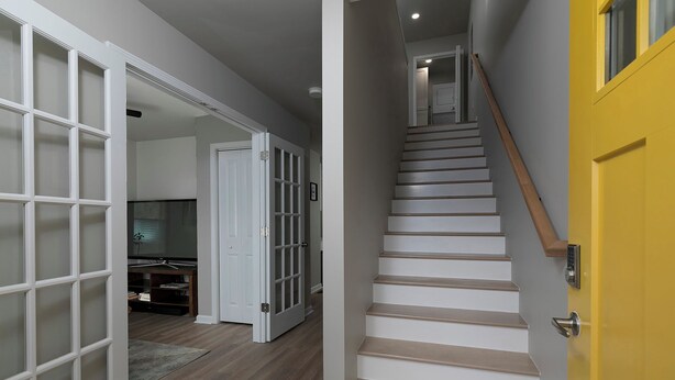 A staircase leading to a landing with a yellow door, a white door with frosted glass panels, and a wooden floor. - Relaxing ATL Getaway • Modern, Clean & Near City Events, Stadiums, & Attractions (Atlanta)