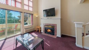 Een woonkamer met een open haard, een televisie erboven en een glazen tafel.