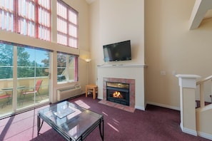 Una sala de estar con chimenea, un televisor montado encima y una mesa de vidrio.